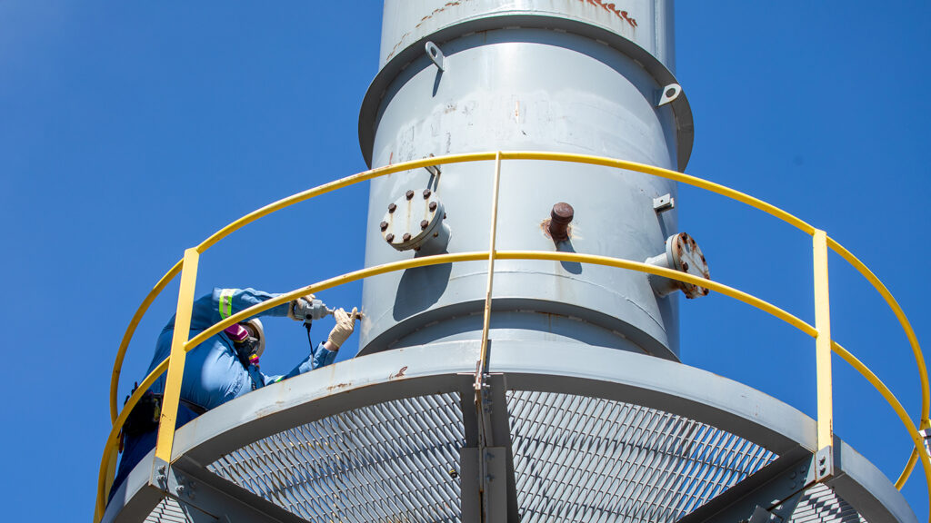 An employee is using a probe to evaluate air emissions from a stack.